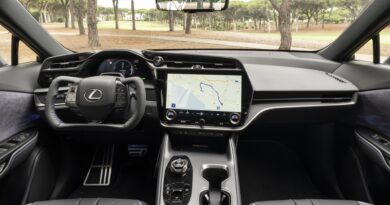 Inside a luxury car cockpit with a large touchscreen navigation system and digital gauge cluster behind the steering wheel.