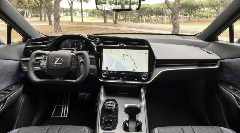 Inside a luxury car cockpit with a large touchscreen navigation system and digital gauge cluster behind the steering wheel.